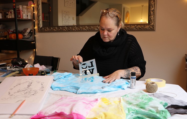 Am Esstisch verziert Nicole Bühler die Shirts mithilfe einer Schablone wie hier mit Love – Liebe. Derzeit tüftelt sie an einem eigenen Sujet (am linken Bildrand): das Friedenszeichen mit Engeln und der Botschaft «never give up» – gib niemals auf. Am Esstisch verziert Nicole Bühler die Shirts mithilfe einer Schablone wie hier mit Love – Liebe. Derzeit tüftelt sie an einem eigenen Sujet (am linken Bildrand): das Friedenszeichen mit Engeln und der Botschaft «never give up» – gib niemals auf.