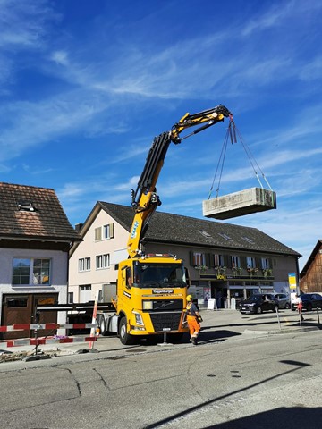 Letzte Woche wurde der alte Brunnen verladen und abtransportiert. Er wird vom bisherigen Standort links des Kranwagens neu vor das Gemeindehaus (rechts hinten) umplatziert werden.