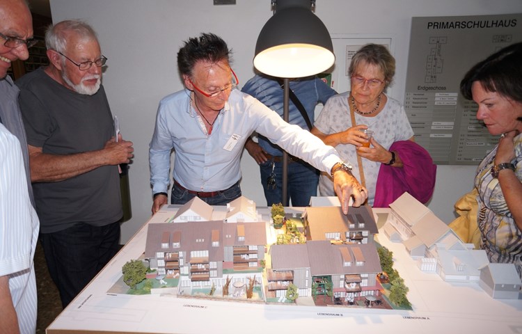 Projektverfasser Kurt Steiner (rote Brille, vor dem Gemeindehaus stehend) hat ein Modell im Massstab 1:100 gebaut. «Sagenhaft» lauteten die Kommentare von begeisterten Genossenschaftern. Das UG erhält Licht durch den vertieften Innenhof (im Bild vorne, Haus links). Projektverfasser Kurt Steiner (rote Brille, vor dem Gemeindehaus stehend) hat ein Modell im Massstab 1:100 gebaut. «Sagenhaft» lauteten die Kommentare von begeisterten Genossenschaftern. Das UG erhält Licht durch den vertieften Innenhof (im Bild vorne, Haus links).